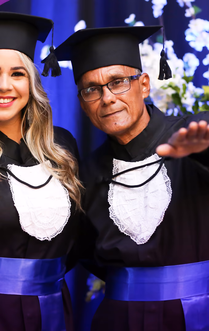 Dois formandos de beca e capelo posam juntos para uma foto durante a cerimônia de colação.